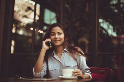 A stock photo of a lady drinking coffee whilst talking on her phone.