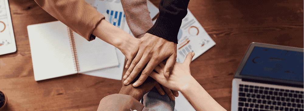 Photo of a team from above looking down, sat around a desk, two of whom are shaking hands in agreement to represent Ethics.